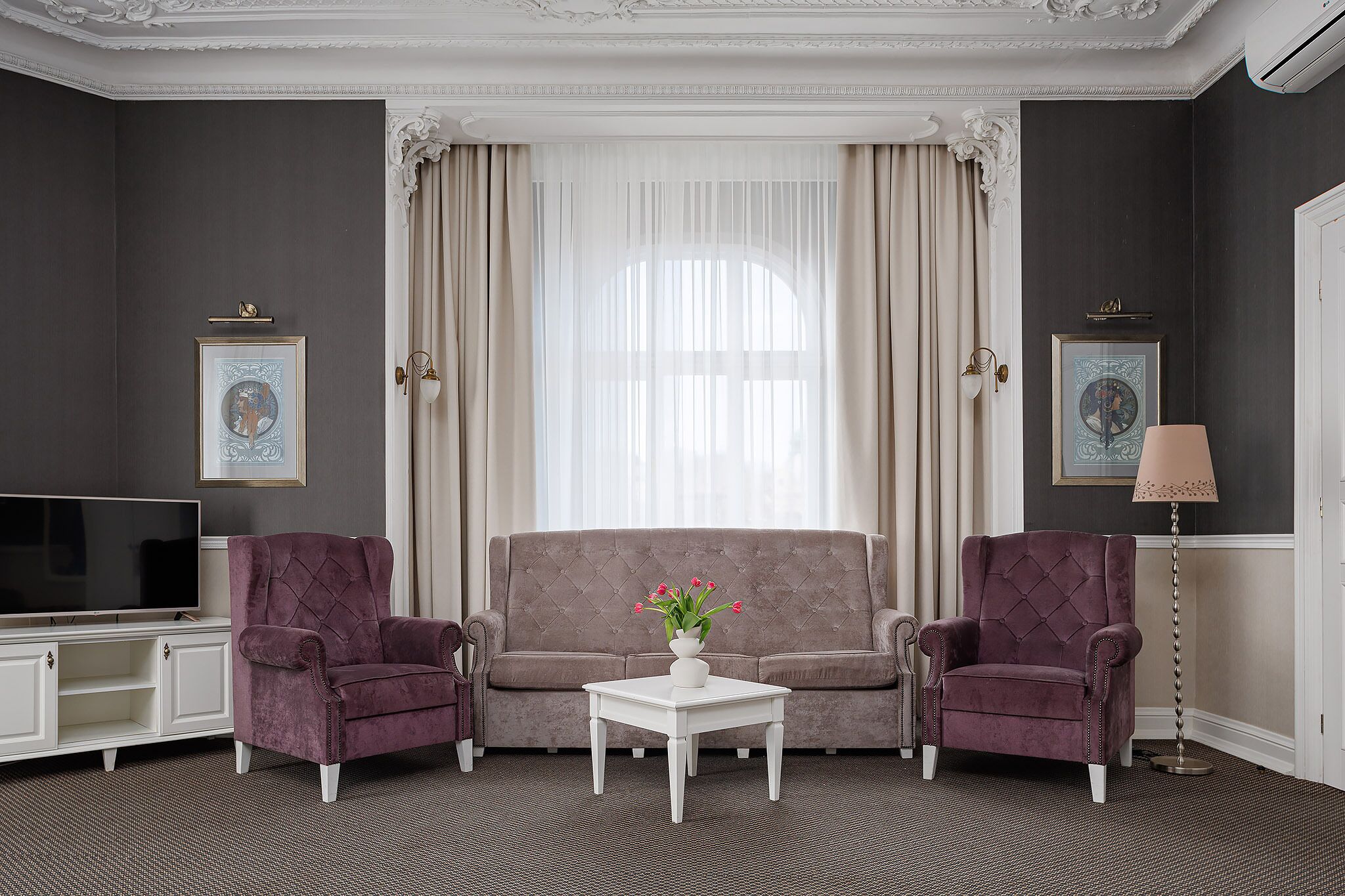 A room with a grey sofa, two armchairs, a white coffee table, a TV, and a lamp.