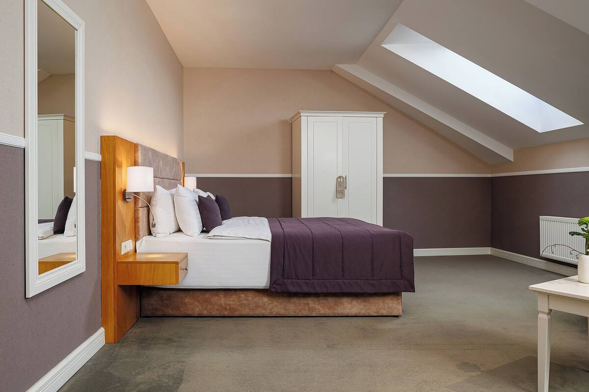A bedroom with a bed, bedside table, lamp, wardrobe, and a skylight.