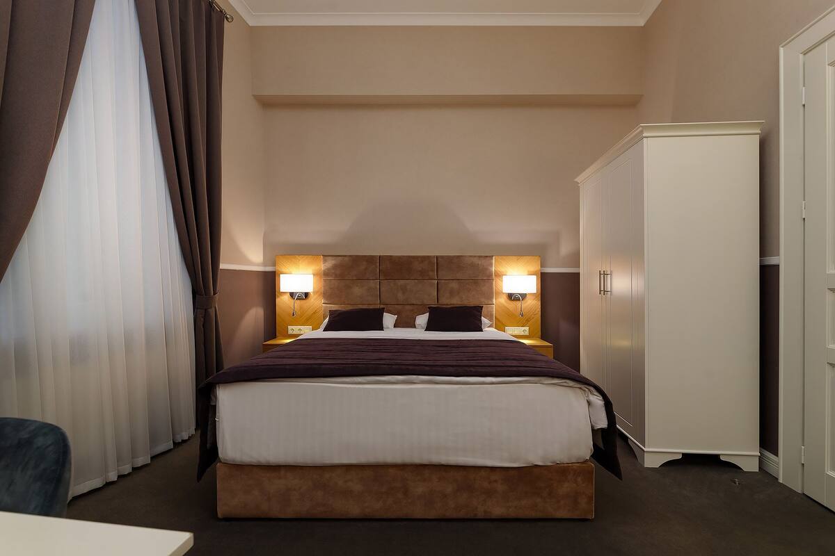 A hotel room with a large bed, two bedside lamps, a wardrobe, and a chair.