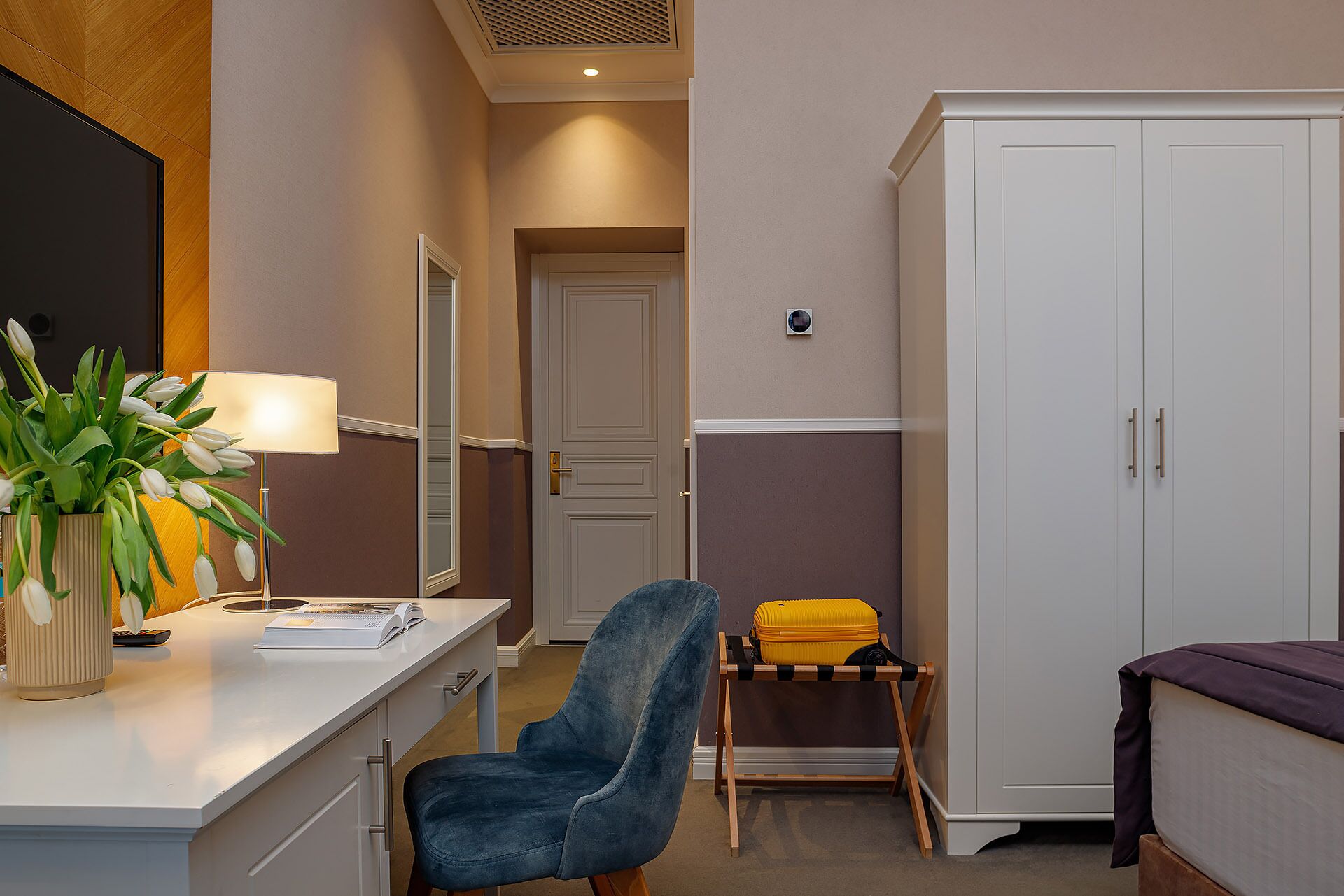 A hotel room with a desk, chair, wardrobe, and a bed.