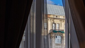 A view through a window with a view of a building with ornate architecture and a balcony. - Modern Art Hotel - Maestro (Lviv)
