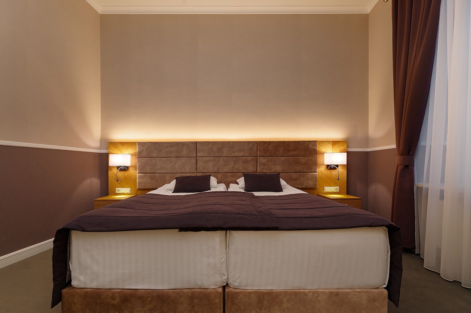 A hotel room with a large bed, two bedside lamps, and a headboard with a light panel.
