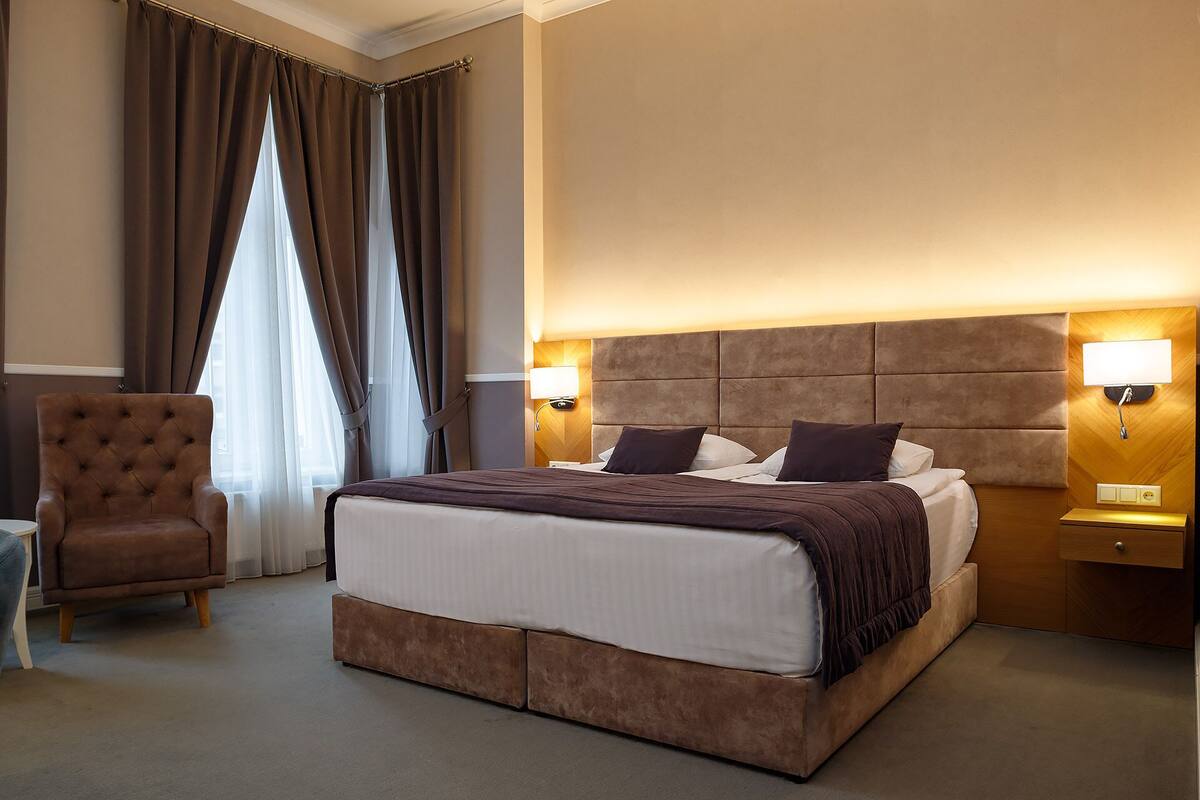 A hotel room with a large bed, a chair, and a nightstand with a lamp.