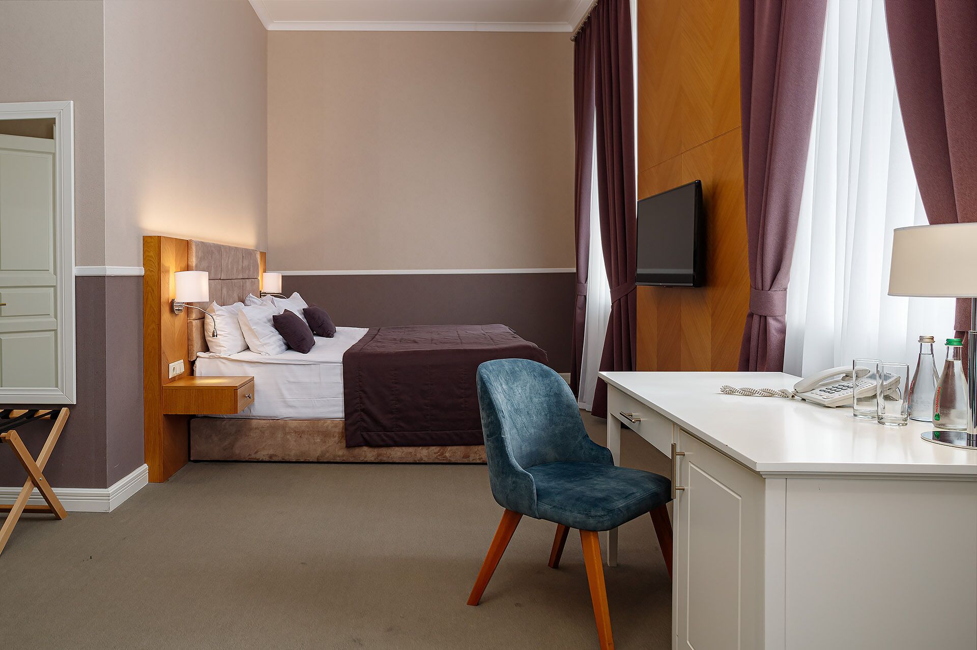 Ein Hotelzimmer mit Bett, Schreibtisch, Stuhl, Fernseher und Nachttisch mit Lampe.