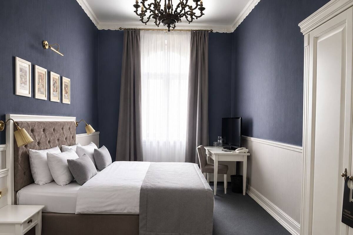 A bedroom with a bed, bedside tables, a desk, a television, and a chandelier.