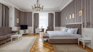 A hotel room with a large bed, a sofa, a TV, a desk, and a chandelier. - Modern Art Hotel - Maestro (Lviv)