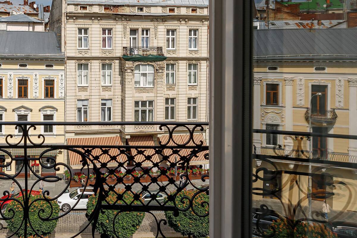 A balcony with wrought iron railings overlooking a street with buildings and parked cars.