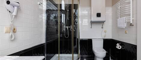 Une salle de bain dotée d’une douche à parois de verre, de toilettes, d’un sèche-cheveux fixé au mur et d’un porte-serviettes.