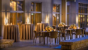 An outdoor dining area with tables and chairs, illuminated by wall-mounted lights. - Hilton Garden Inn Foxborough Patriot Place (Foxborough)