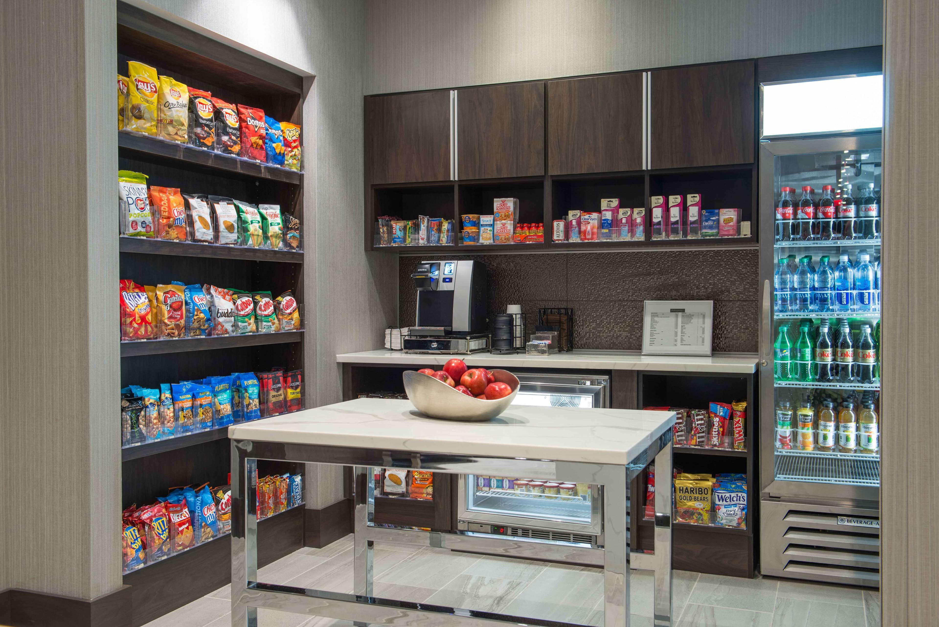 A self-service snack and beverage station with shelves stocked with various snacks and a refrigerated section with bottled drinks.