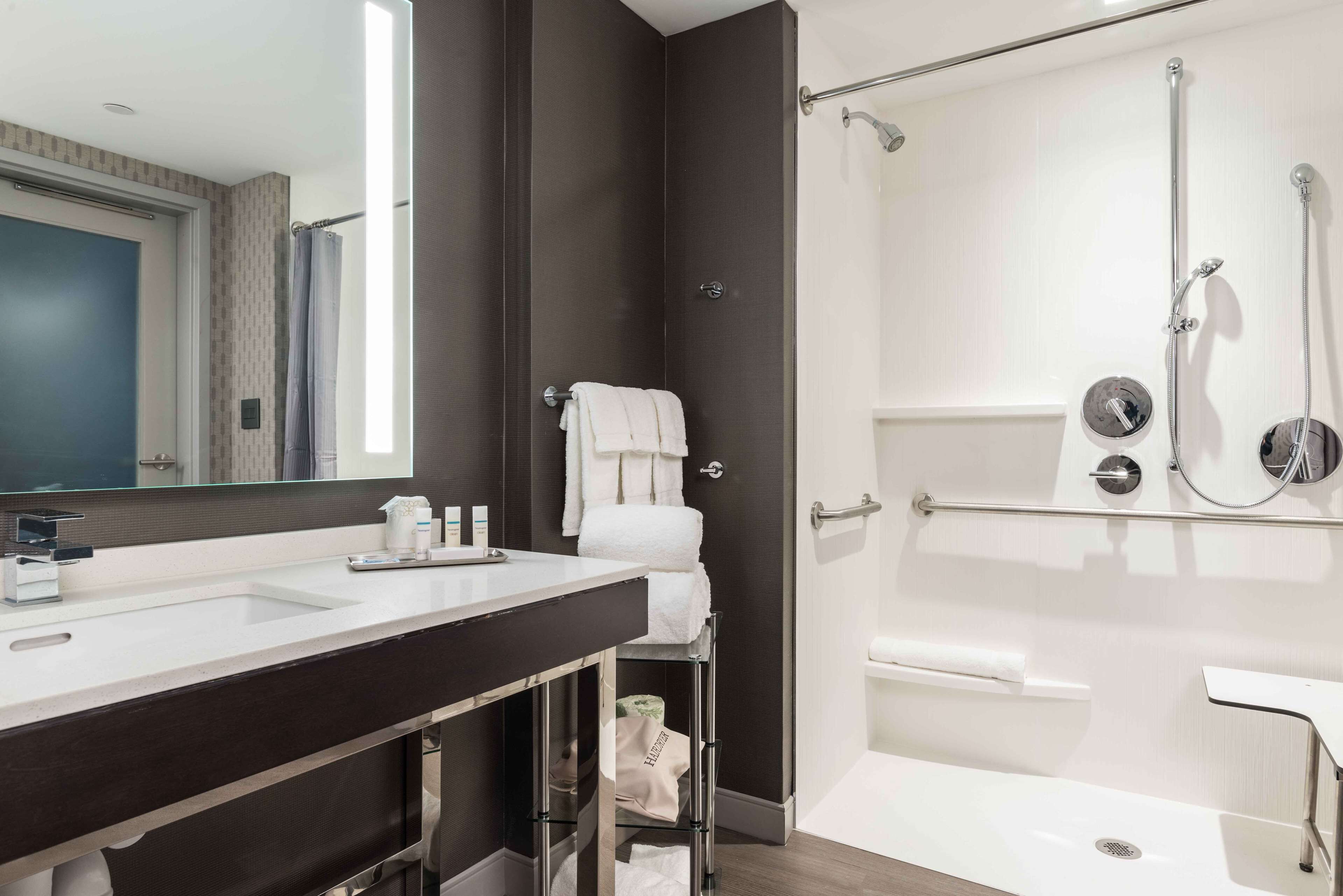Ein modernes Badezimmer mit einem Doppelwaschbecken, einem großen Spiegel, einer Dusche mit Glastür und einem Handtuchhalter.