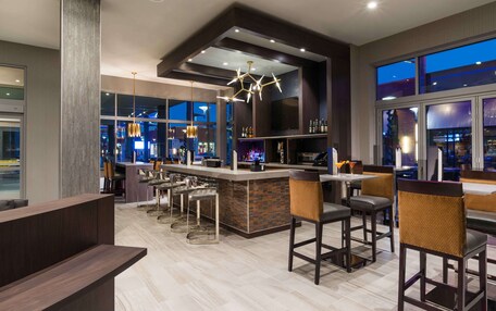 A modern bar area with a bar counter, stools, and a large window overlooking the city.