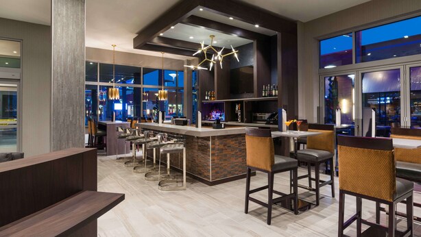 A modern bar area with a bar counter, stools, and a large window overlooking the city. - Hilton Garden Inn Foxborough Patriot Place (Foxborough)