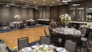 Un salón de conferencias de hotel con mesas redondas, sillas y centros de mesa florales.