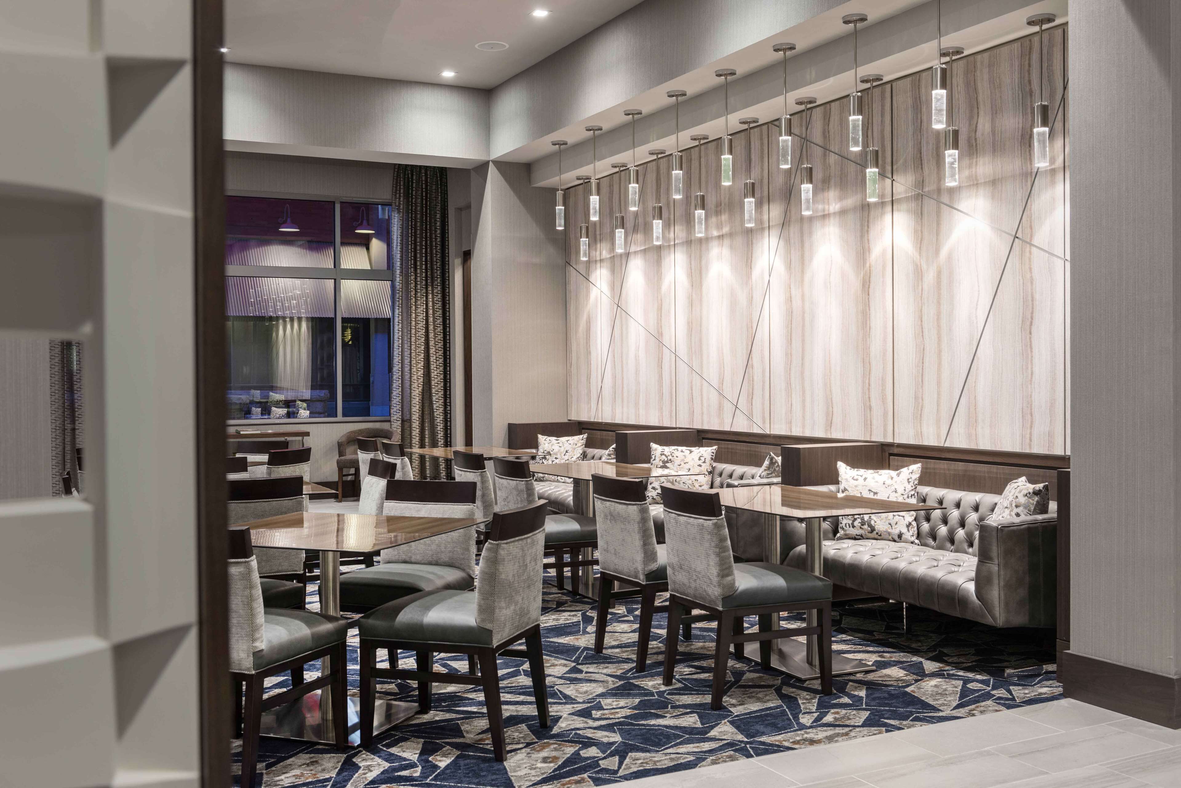 A modern dining area with a mix of tables and a sofa, featuring a geometric patterned carpet and a wall with a light wood finish.