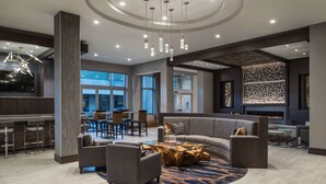 A modern hotel lobby with a curved sofa, a coffee table, and a bar area with stools. - Hilton Garden Inn Foxborough Patriot Place (Foxborough)