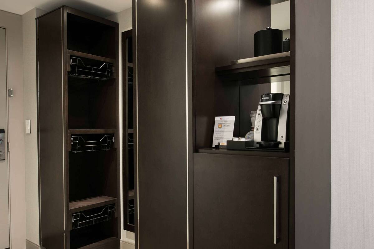 Een moderne kamer met een donkerhouten kast, een koffiezetapparaat en een klein plankje met een bordje.