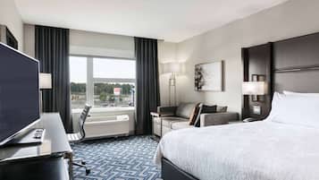 A hotel room with a bed, a desk with a computer, a sofa, a TV, and a window with curtains.