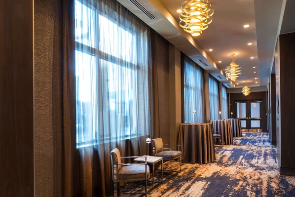 Un hall de hotel con ventanas amplias, piso alfombrado y luminarias modernas.