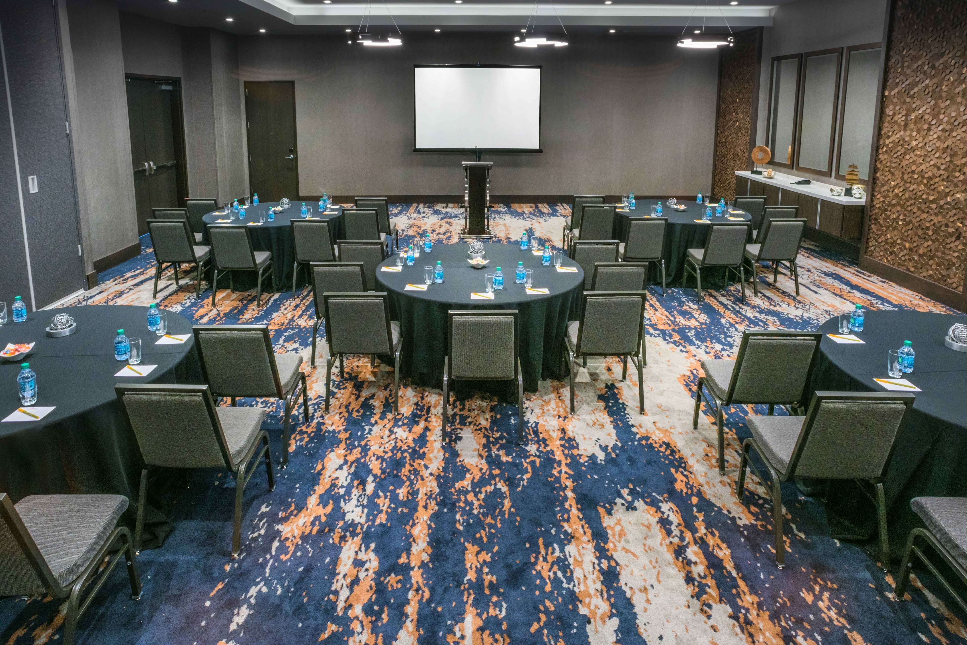 A conference room with a large screen, multiple tables with chairs, and water bottles.