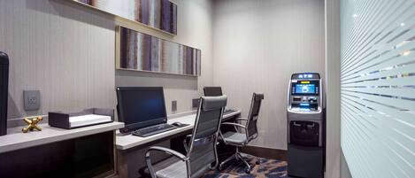 A hotel room with a desk, two chairs, a TV, and an ATM.