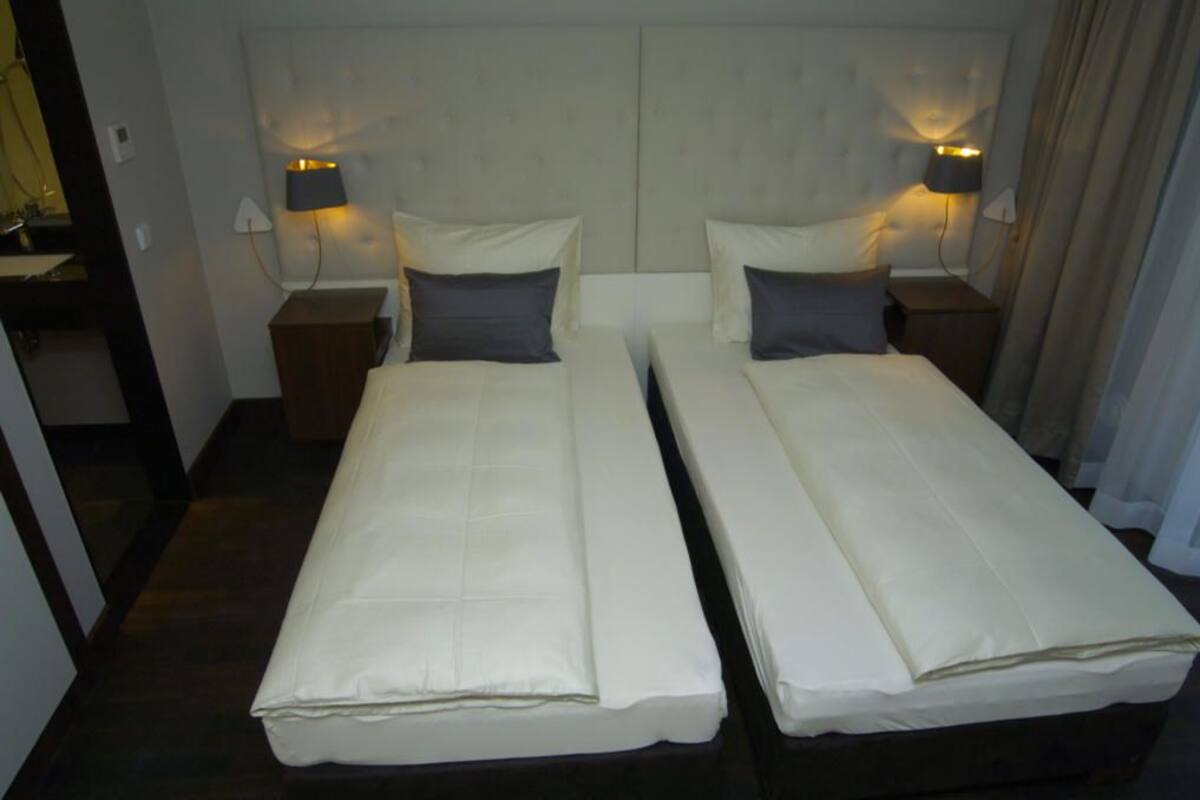 Une chambre double avec deux lits simples, chacun étant équipé d’un oreiller et d’une table de chevet avec une lampe.