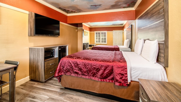 A hotel room with a bed, a TV, a desk, and a ceiling mural.