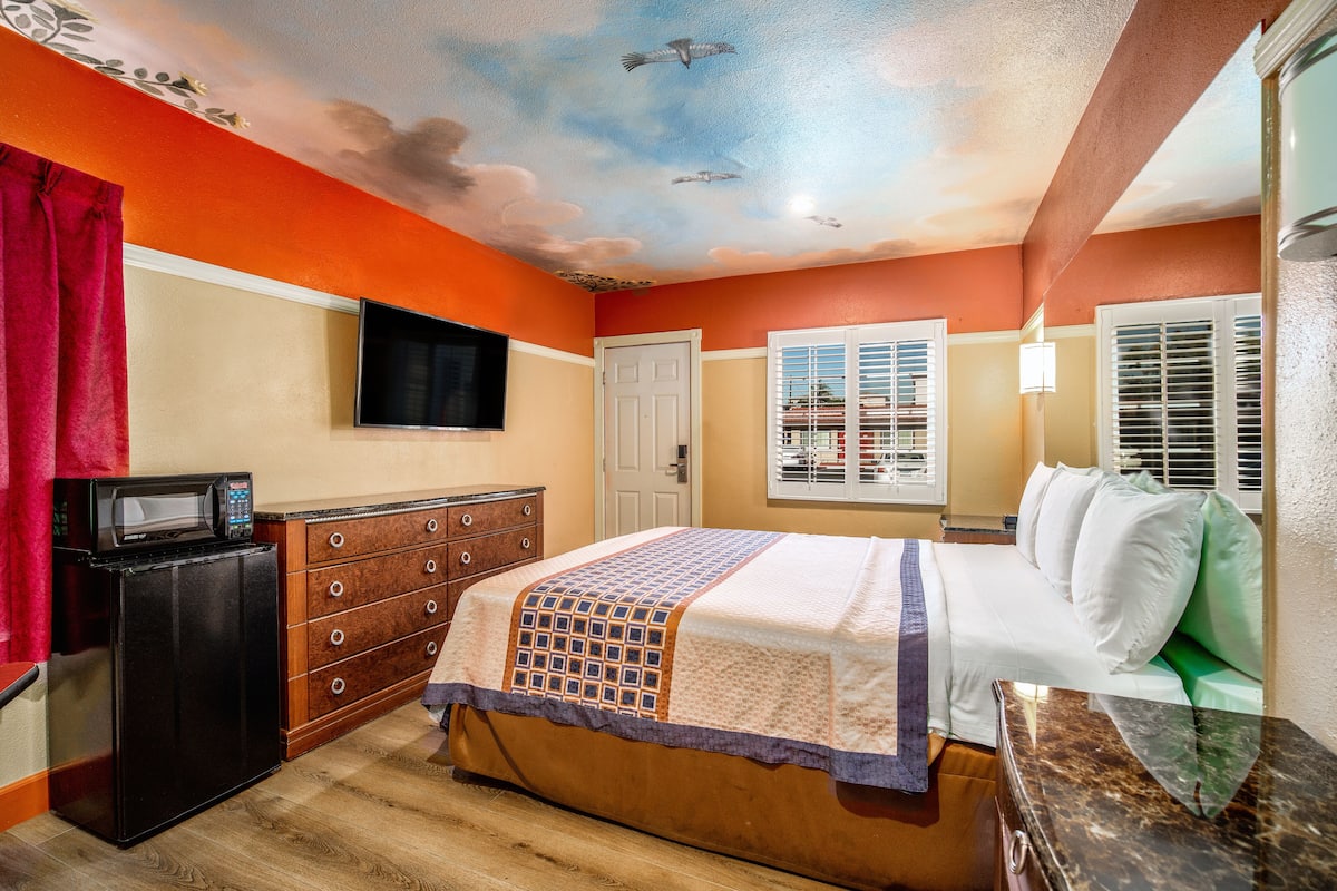 A hotel room with a bed, a dresser, a microwave, a TV, and a window with blinds.