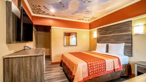 A hotel room with a bed, a mirror, a TV, and a wooden cabinet.