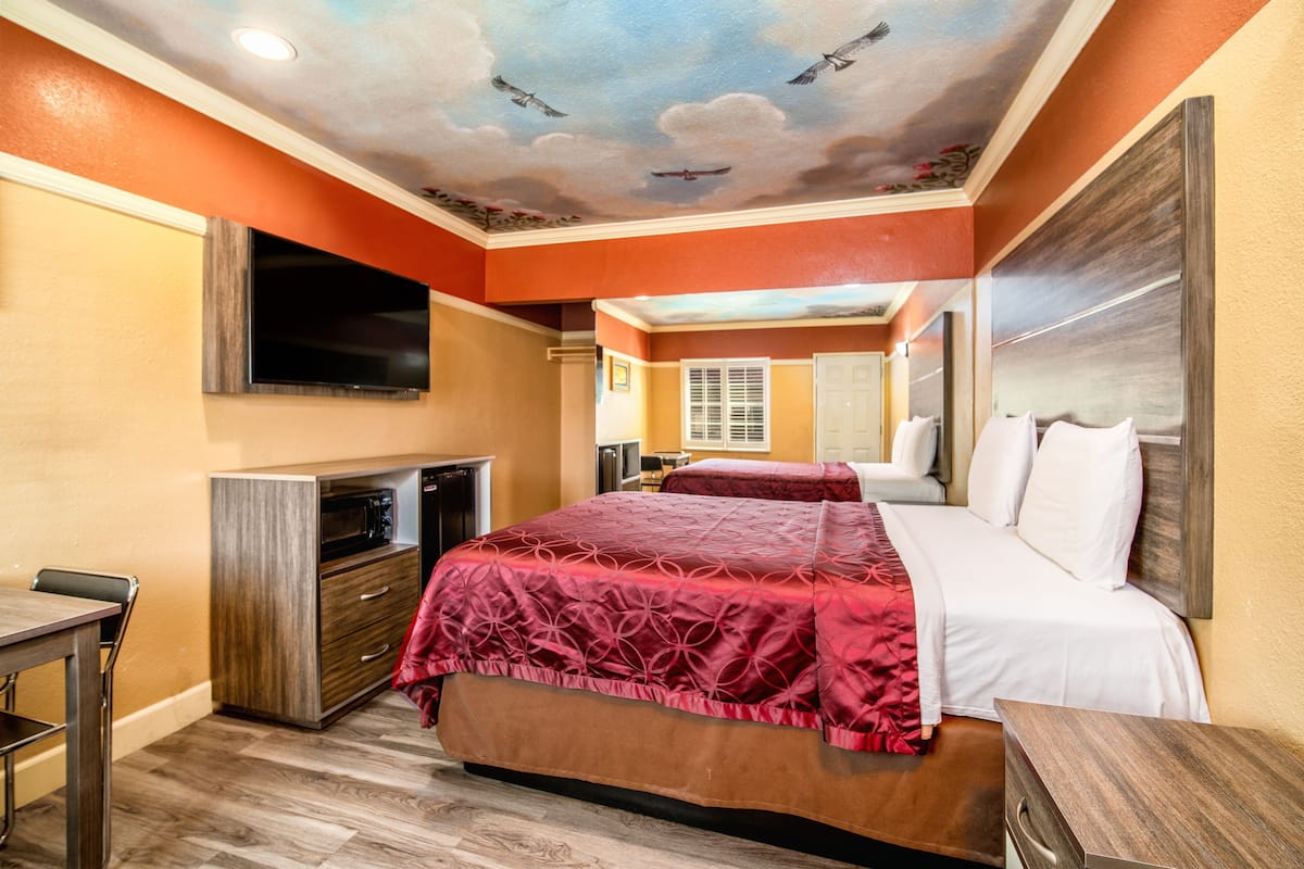 A hotel room with a bed, a TV, a desk, and a ceiling mural.