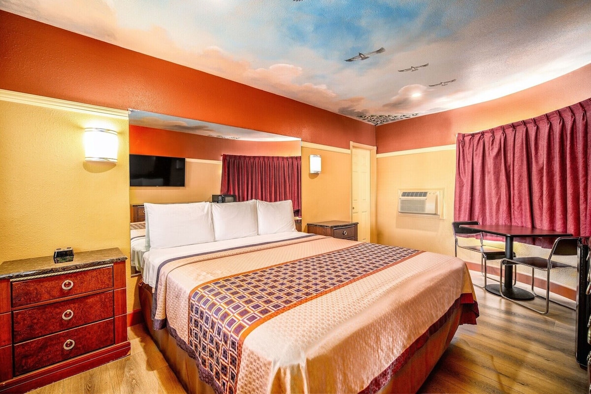 A hotel room with a bed, a desk, a chair, a dresser, and a television.