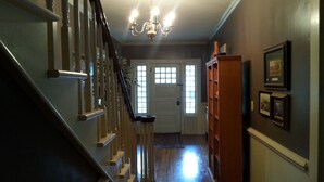 Una escalera con un candelabro, una puerta de madera con paneles de vidrio y una estantería de madera con cuadros enmarcados.