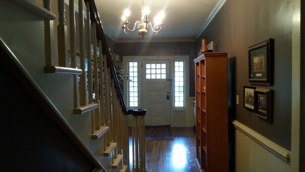 A staircase with a chandelier, a wooden door with glass panels, and a wooden bookcase with framed pictures. - Hunter House Bed and Breakfast (Madison)
