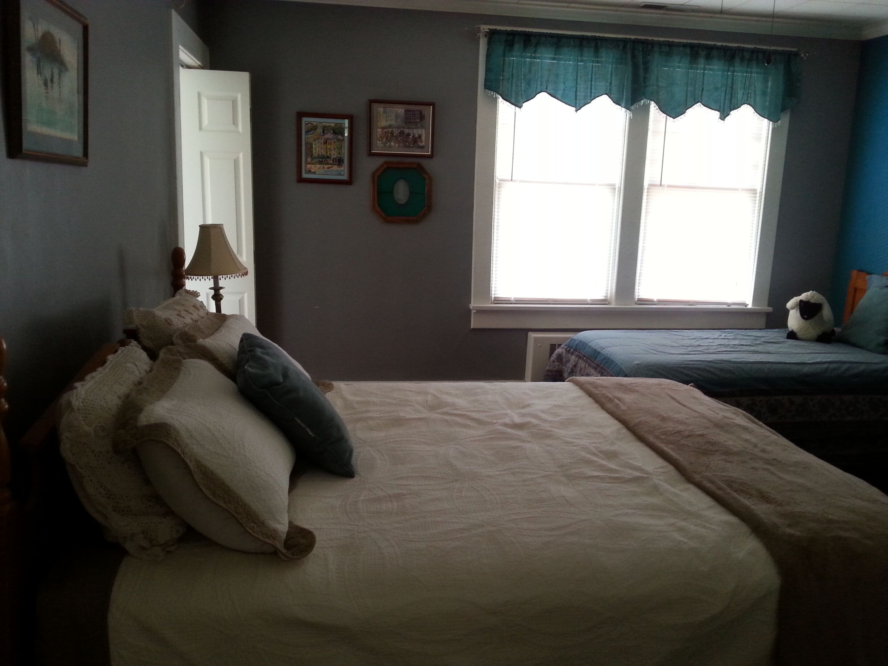 Une chambre avec deux lits, une fenêtre avec des rideaux et des tableaux encadrés accrochés au mur.