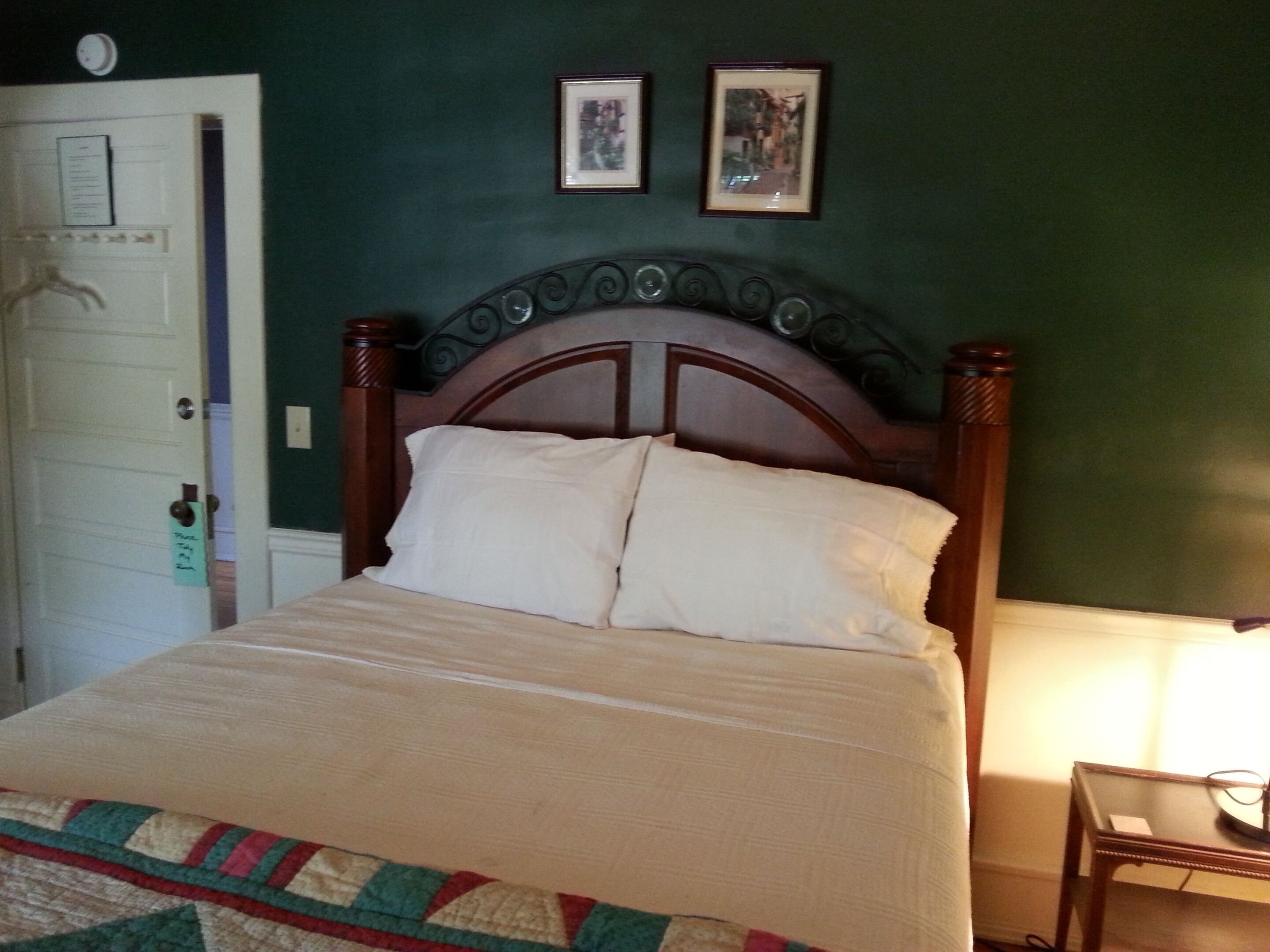 A bedroom with a wooden bed, a quilt, and two framed pictures on the wall.