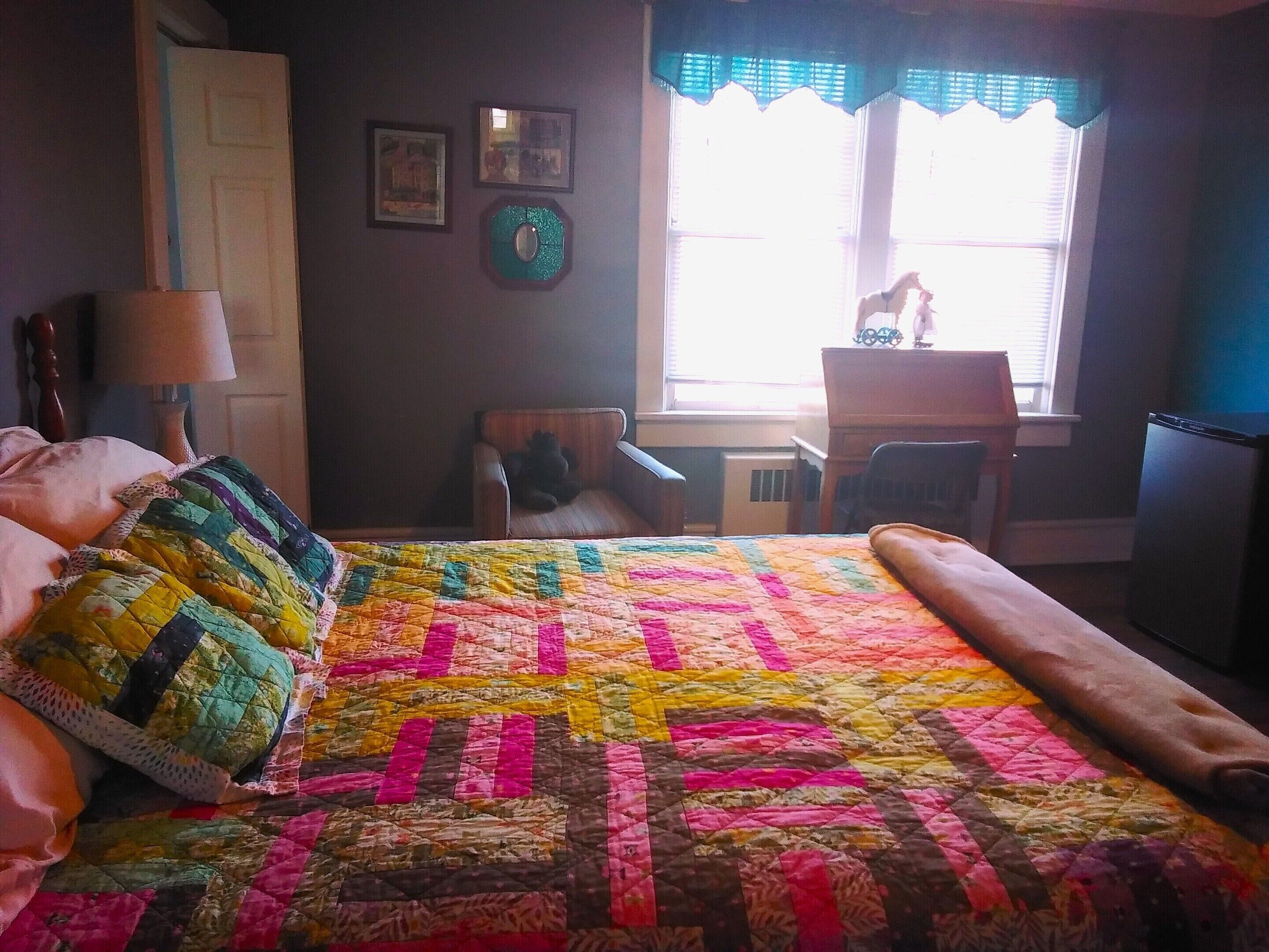 A bedroom with a large bed, a chair, a desk, and a window with curtains.