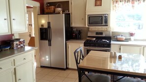 A kitchen with white cabinets, a stainless steel refrigerator, a microwave, a stove, and a dining table with chairs. - Hunter House Bed and Breakfast (Madison)