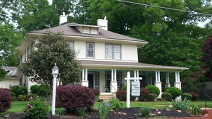 A two-story house with a porch, surrounded by a brick wall and various plants. - Hunter House Bed and Breakfast (Madison)