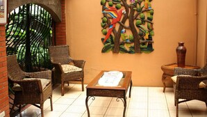 A room with wicker furniture, a glass-top table, and a mural of colorful birds on a tree. - Hotel Millenium (Rio Segundo)