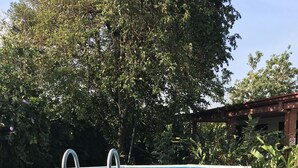 An above-ground swimming pool with a ladder, surrounded by lush greenery and a wooden structure in the background. - Hotel Millenium (Rio Segundo)