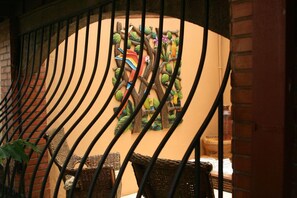A staircase with a wrought iron railing, a wall with a colorful mural of birds and foliage, and wicker furniture. - Hotel Millenium (Rio Segundo)