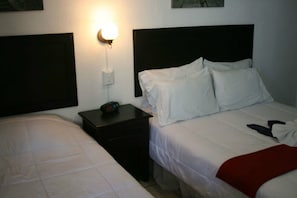 Een hotelkamer met twee bedden, een nachtkastje met een klok en een wandlamp.