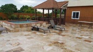 Un patio al aire libre con piscina, sillas de descanso y una zona de estar cubierta.