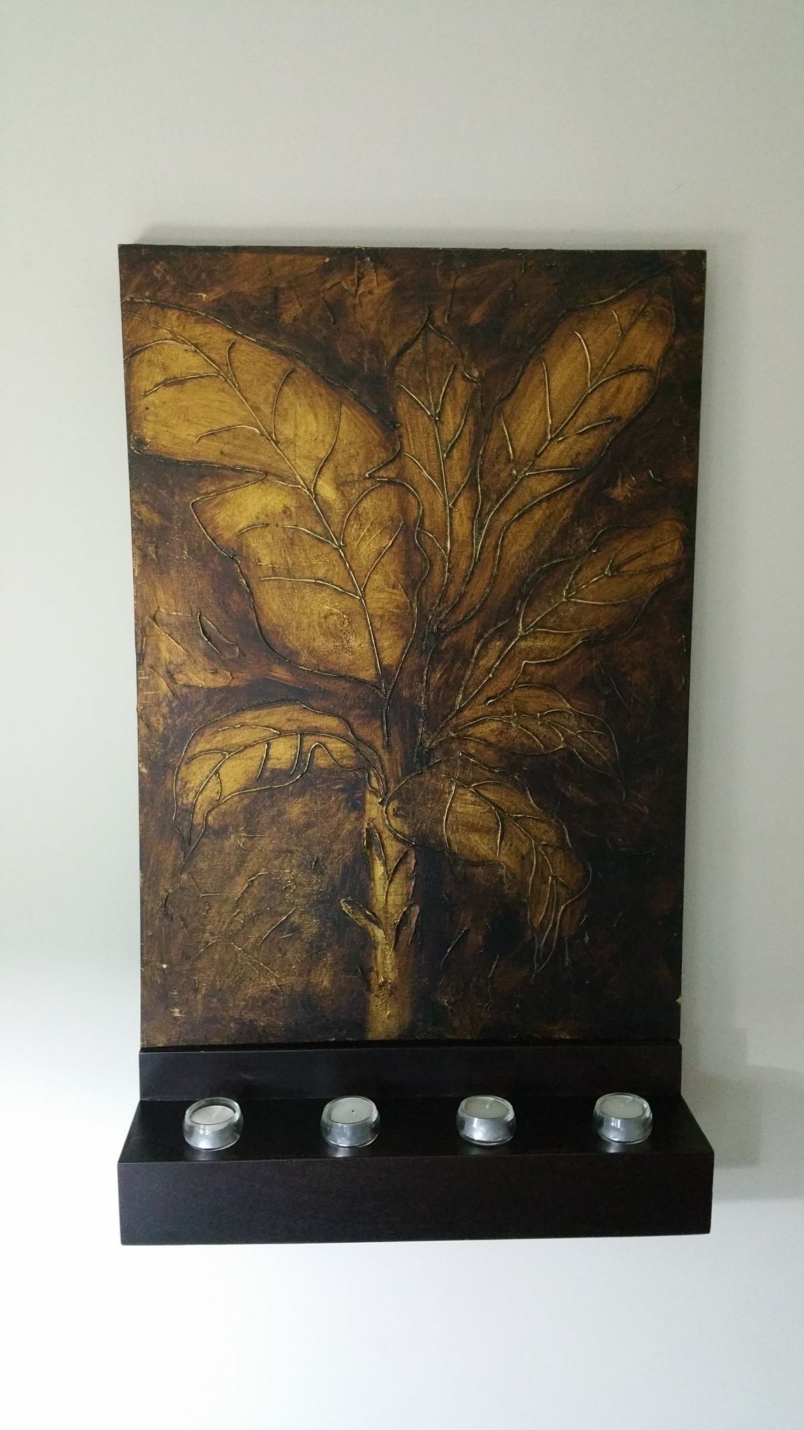 Une peinture représentant un arbre aux feuilles, posée sur une étagère noire.