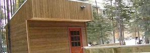 A wooden cabin with a red door, surrounded by trees. - Castle Mountain Ski Lodge - Hostel (Castle Mountain Resort)