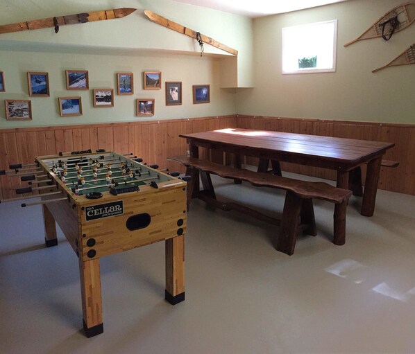 A room with a foosball table, a wooden bench, and a wall with framed pictures.