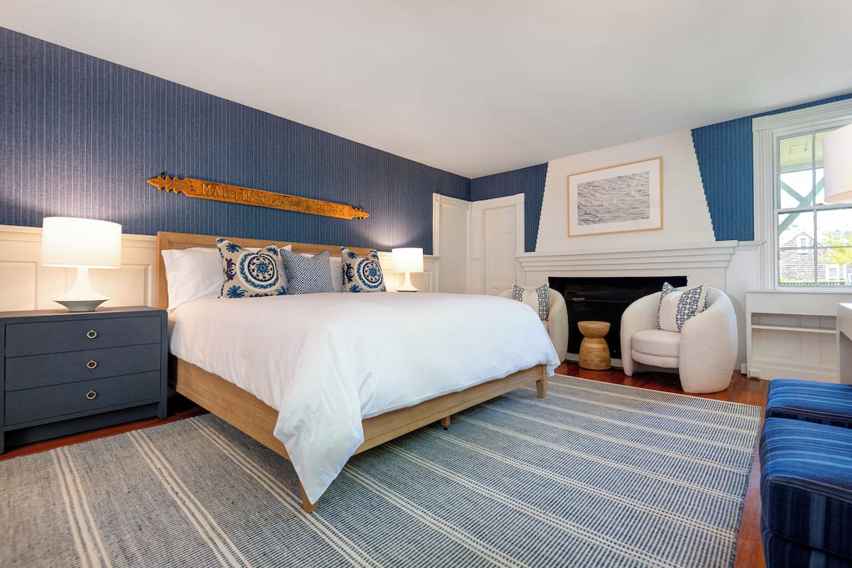 A bedroom with a large bed, two bedside tables with lamps, a fireplace, and a window with curtains.