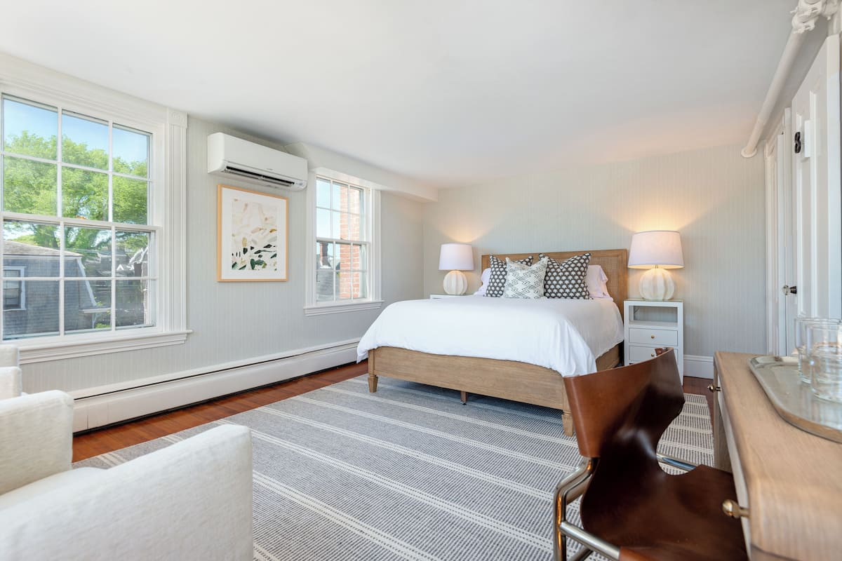 A bedroom with a large bed, two bedside tables, a chair, and a window with a view of trees.