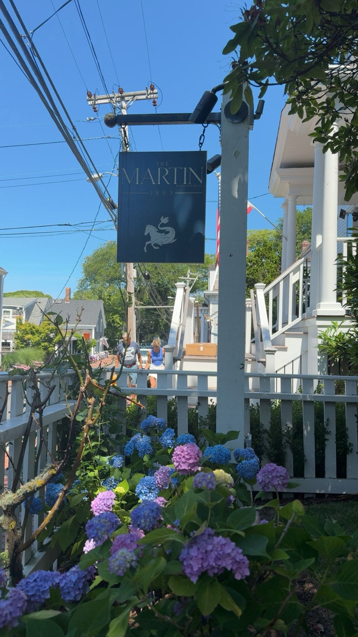 A sign for 'The Martin' pub with a horse emblem, surrounded by a white fence and hydrangea flowers.