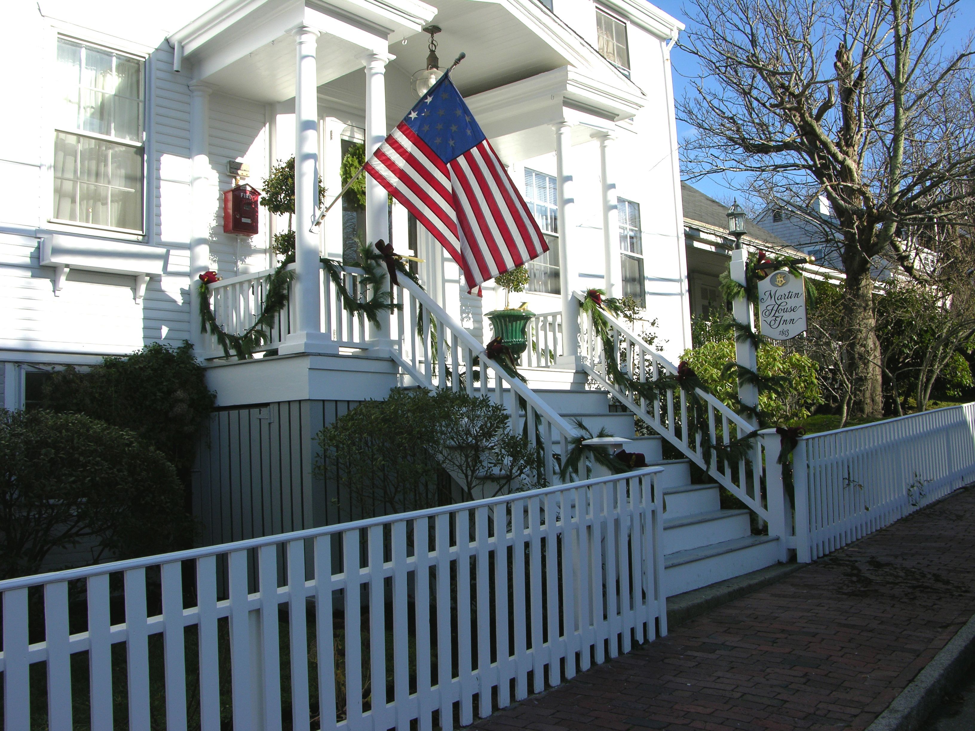 A white colonial-style building with a front porch, a staircase, and a flag.